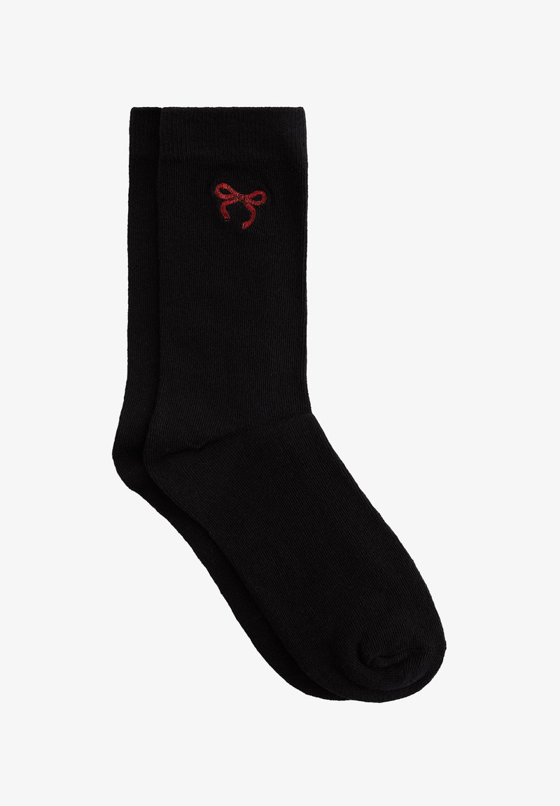 Črne nogavice iz mehkega, raztegljivega blaga z gladko teksturo. Imajo majhen rdeč lok logotip blizu robu. Klasična zasnova do kolen.