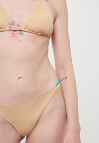 Top bikini beige con coppe triangolari e dettagli arricciati. Il bottom coordinato presenta accenti laterali multicolori in blu e giallo.