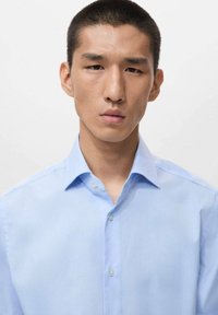 Light blue button-up shirt with a spread collar and visible buttons. Smooth fabric texture, tailored fit, and minimal design details.