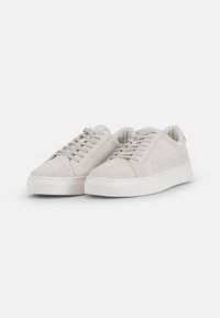 Vaaleanharmaat mokkanahkaiset sneakerit, joissa on matala muotoilu, pyöreä kärki ja valkoinen kumipohja. Varustettu tasaisilla nauhoilla ja minimalistisilla ompeleilla.