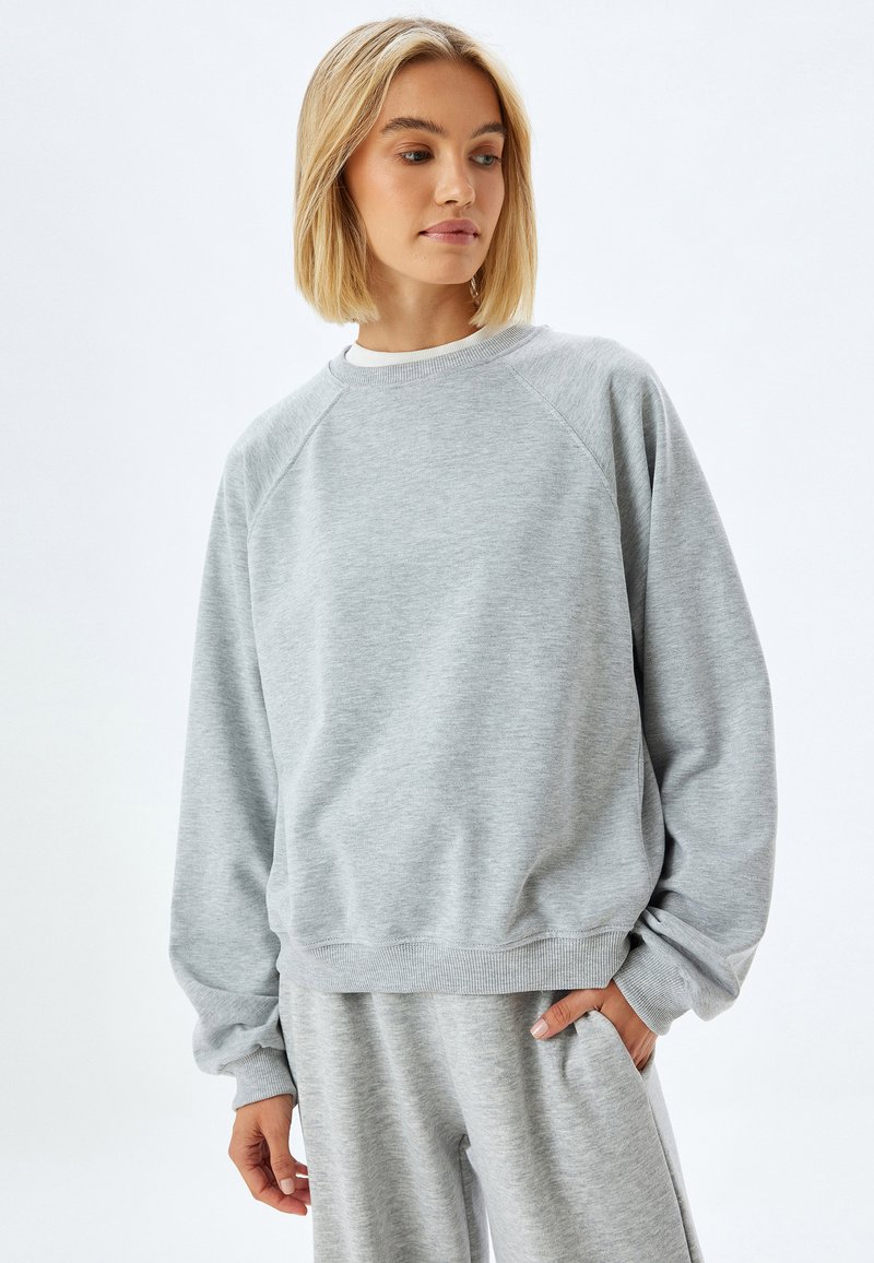 Grijze sweatshirt van zacht materiaal; heeft raglan mouwen en geribbelde manchetten, met een relaxte pasvorm en een ronde halsontwerp.