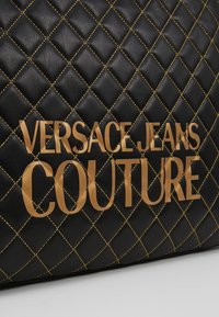 Surface en cuir matelassé noir avec coutures dorées et texte doré indiquant Versace Jeans Couture.