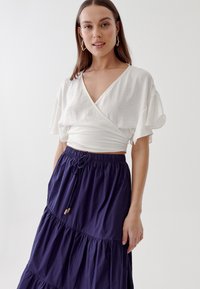 Top bianco avvolgente con maniche corte a campana abbinato a una gonna maxi a strati blu navy. La gonna è dotata di una vita elastica e di un laccetto.