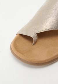 Μεταλλικό δερμάτινο σανδάλι σε ανοιχτό χρυσό με θηλιά για το δάχτυλο, μαλακό μπεζ σουέτ πέλμα και στρο γγυλεμένη εξωτερική σόλα για άνεση.