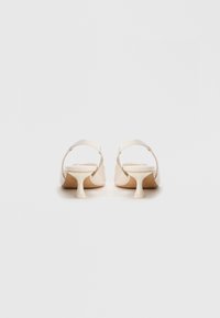 Sapatos de salto aberto bege com bico arredondado, salto fino e tiras texturizadas. Superfície lisa e brilhante com design minimalista.