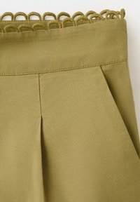 Tissu vert olive avec une ceinture cousue et une bordure décorative bouclée le long du bord supérieur, présentant un pli vertical et une poche latérale.