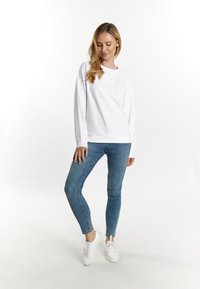 Pulover alb cu maneci lungi, asortat cu blugi skinny de culoare albastru deschis și adidași albi. Material neted, guler clasic și design ajustat.