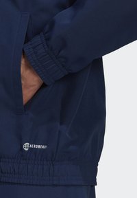 Navyblauwe jas met elastische manchetten, met een gladde textuur en een zijzak. Heeft een "AEROREADY" label op de zoom.