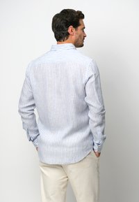 Pasiasta koszula z długim rękawem w jasnoniebieskim i białym kolorze, z kołnierzykiem zapinanym na guziki, zaokrąglonym dołem i detalem w postaci yoku na klatce piersiowej.