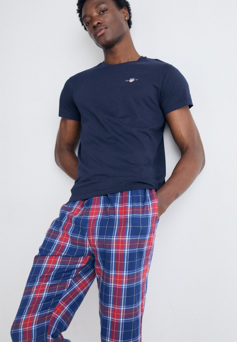Navy Baumwoll-T-Shirt mit kleinem Logo auf der Brust, kombiniert mit blau-roten karierten Flanellhosen mit elastischem Bund.
