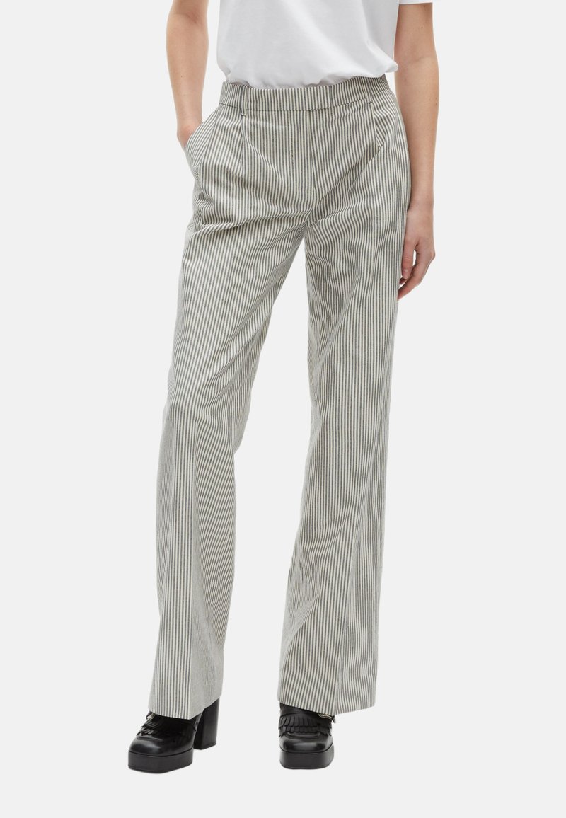 Pantalons taille haute à rayures grises et blanches avec des plis, des poches latérales et une coupe droite, associés à des chaussures à plateforme noires.