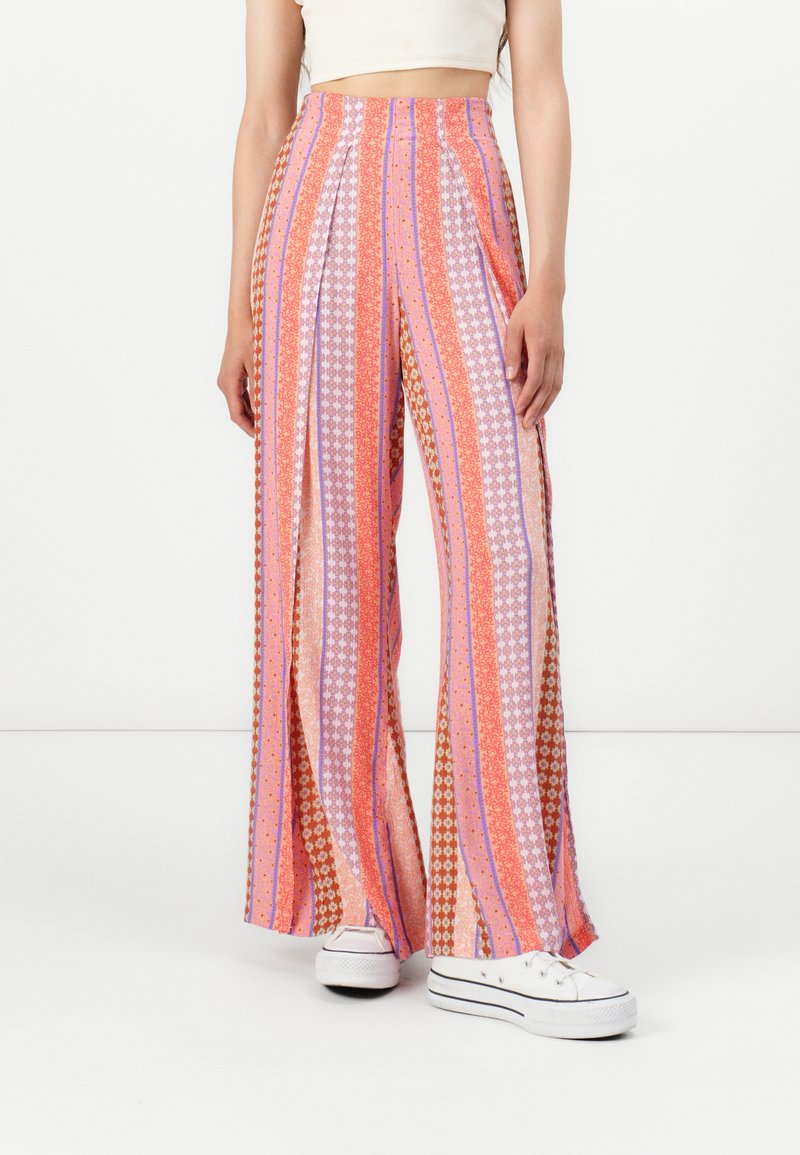 Pantalons larges avec un mélange de rayures roses, violettes et orange, ornés de motifs floraux. Fabriqués dans un tissu léger, conçus pour le confort.