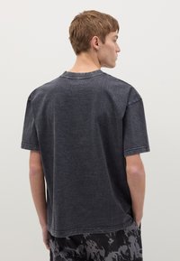 Camiseta de manga corta en gris oscuro con cuello redondo, que presenta un acabado texturizado y costuras visibles. La tela es suave y casual.