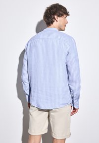 Lichtblauw gestreepend shirt van zachte stof, met een gebogen zoom en knoopmanchetten, gecombineerd met opgerolde beige shorts.