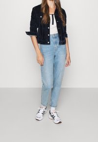 Námořnická sametová zkrácená bunda, bílý top na ramínka, světle modré džíny s vysokým pasem a bílé tenisky s černými akcenty a oranžovým logem.