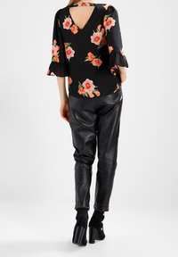 Černá květinová blůza s volánovými rukávy, má výstřih do V a otevřený zadní díl. Kombinována s černými koženými kalhotami a botami na podpatku.