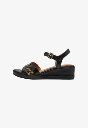 Sandale compensée en cuir noir avec accent imprimé léopard, bride de cheville réglable, bout ouvert et semelle texturée. Présente un détail de boucle dorée.