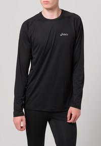 Svart långärmad träningsskjorta gjord av fukttransporterande material, med rund halsringning och reflekterande logotyp på övre vänstra bröstet.