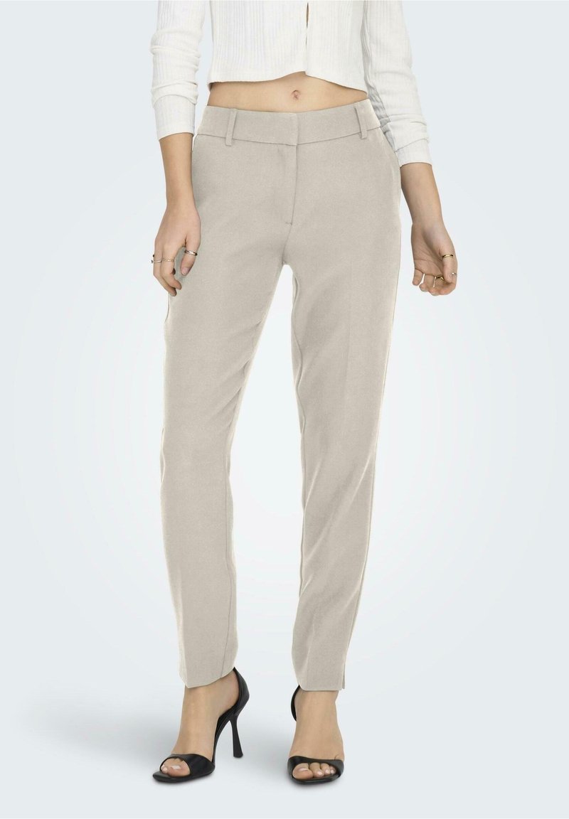 Pantalons beige ajustés avec une coupe slim, devant plat et passants de ceinture. Dispose de poches latérales et d'une texture de tissu lisse. Talons ouverts noirs.