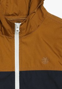 Giacca bicolore marrone e blu navy con chiusura a zip, realizzata in un tessuto testurizzato e con un piccolo logo sul petto.