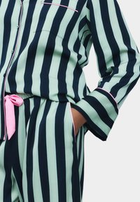 Set di pigiama a righe in verde menta e blu navy, con un fiocco rosa in vita, una tasca sul petto e polsini in contrasto.