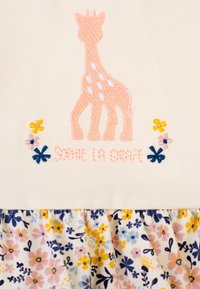 Tessuto crema con ricamo di una giraffa rosa e dettagli floreali. Gonna floreale con fiori gialli, blu e rosa, caratterizzata da un orlo arricciato.