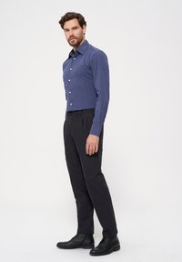 Ciemnoniebieska koszula z długim rękawem i guzikami w zestawie z czarnymi spodniami i czarnymi sznurowanymi butami, o dopasowanym kroju i gładkiej fakturze.