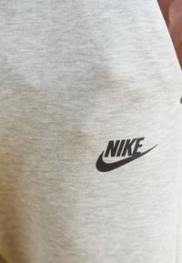 Šedá bavlněná tkanina s hladkou texturou, na které je výrazně zobrazeno černé logo Nike. Jednoduchý a funkční design.