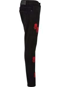 Melni denima džinsi ar šauru piegriezumu, ar sarkano skeletu un krustotām kaulu izšuvumu katras kājas ārējā pusē.