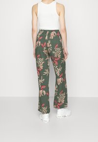 Květnaté široké kalhoty v tmavě zelené látce, s červenými a béžovými vzory květin a motýlů, s elastickým pasem pro pohodlí.