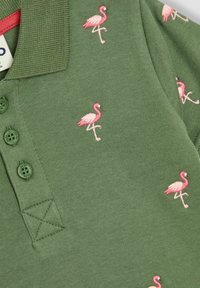 Vihreä poolopaita, jossa on kolme vihreää nappia, pinkin flamingon brodeeraus, pehmeä kangas ja lyhyet hihat klassisella kauluksella.