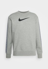 Ljusgrå långärmad sweatshirt med en svart Nike-swoosh på bröstet och märkesremen som löper ner längs ärmarna.