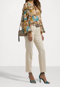 Květinová blůza s nafouknutými rukávy v béžové, modré a zelené barvě. Krémové kalhoty rovného střihu. Tyrkysové sandály na vysokém podpatku a malá šedá kabelka.
