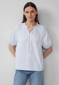 Blouse rayée bleu clair et blanche avec des manches courtes bouffantes, un col froncé et un détail en pointe. Tissu en coton avec une légère texture.