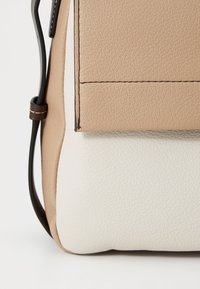 Borsa in pelle testurizzata beige e bianca con chiusura a pattina, caratterizzata da cuciture a contrasto e un design elegante. Minimalista e funzionale.