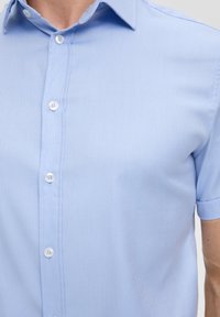 Jasnoniebieska, krótko rękawowa koszula z teksturowanej tkaniny z delikatnym wzorem. Posiada klasyczny kołnierzyk i białe zapięcia na guziki.