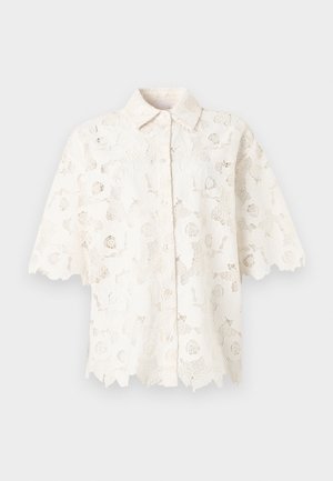 Fehér csipke rövid ujjú blúz virágmintákkal, gombos elől, hullámos szegélyekkel és klasszikus gallérral.