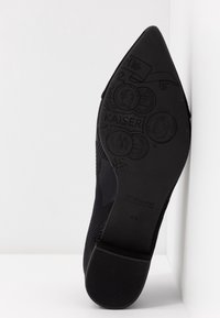 Chaussure noire à talon haut avec un bout pointu. La semelle présente des détails embossés, y compris la marque « KAISER » et des motifs décoratifs.