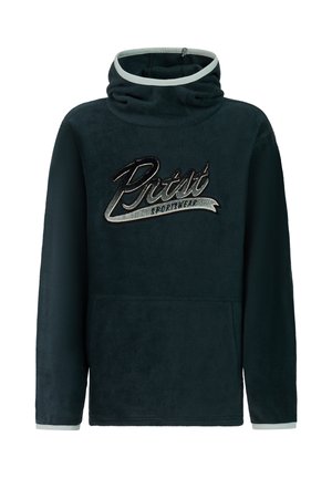 Jongen die een zwarte zonnebril draagt, een donkergroene hoodie met de tekst "Pistist Sportswear", lichtgrijze skibroek en zwarte laarzen, staand tegen een effen achtergrond.