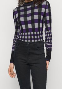 Pull à carreaux noir et gris avec des accents violets, des poignets côtelés et une coupe ajustée, assorti à un jean en denim foncé.