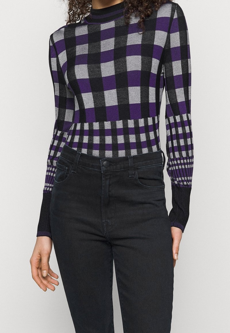 Pull à carreaux noir et gris avec des accents violets, des poignets côtelés et une coupe ajustée, assorti à un jean en denim foncé.