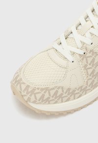 Beige sneakers med overdeler av mesh-stoff, teksturerte detaljer og tonale merkeakenter. Hvite snørebånd og en gummisåle fullfører designet.