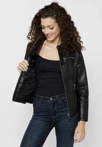 Black leather jacket with a fitted design, zippered front, and ribbed shoulder accents, worn over a black tank top. Clear stitching and pockets visible.