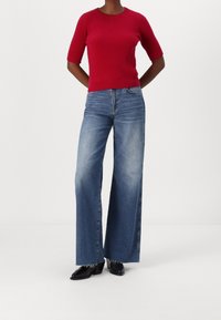 Roter gerippter Kurzarm-Pullover kombiniert mit hellblauen weit geschnittenen Jeans. Schwarze ankle boots mit Absätzen betonen das Outfit.