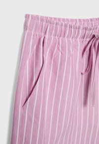 Pantalons rayés roses en tissu léger, dotés d'une taille élastique, d'un cordon de serrage et de poches latérales. Les rayures sont blanches et verticales.