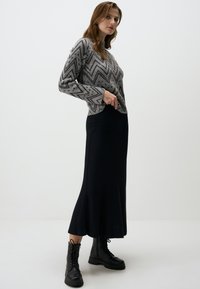 Pull en tricot gris à motif chevron, associé à une jupe maxi noire à côtes et des bottines à lacets noires. Silhouette simple et ajustée.