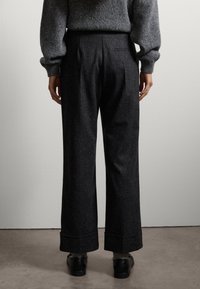 Wijde pijpen broek in donkergrijze stof, met een gladde textuur, omgeslagen manchetten en een hoge taille. Ze hebben achterzakken en plooien.