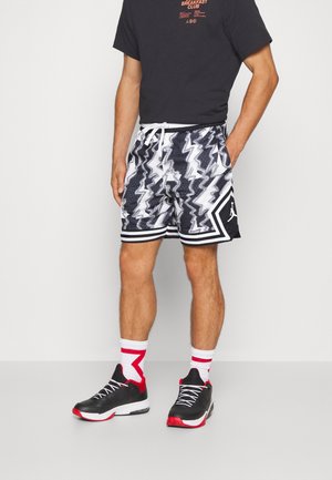 Sort-hvide shorts med zigzag mønster, snor i taljen, sidelommer og kontrastfarvede sort-hvide striber. Sorte sneakers med røde detaljer.