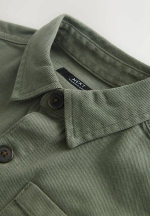 Kaelus ja oliivrohelise nügimisnööbiga särgi ülaosa, millel on tume nööp ja õmmeldud tasku, krae sees on silt "NEXT".