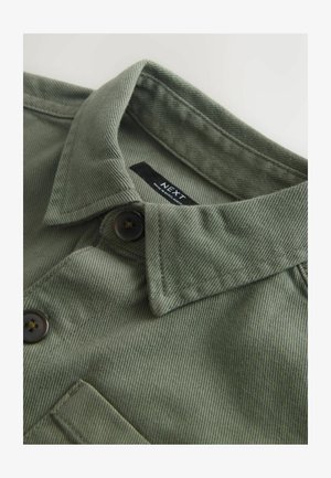 Colletto e parte superiore frontale di una camicia verde oliva con bottoni scuri e tasca cucita, con etichetta "NEXT" all'interno del colletto.